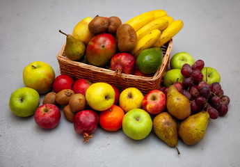 Fruit basket with different fruits. Vitamin set of a healthy diet. Fruit isolated on a gray background. Large set of fruits on a wooden kitchen table. Bananas, apples, pears, pomegranate, tangerine.