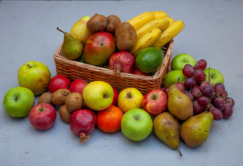 Fruit basket with different fruits. Vitamin set of a healthy diet. Fruit isolated on a gray background. Large set of fruits on a wooden kitchen table. Bananas, apples, pears, pomegranate, tangerine.