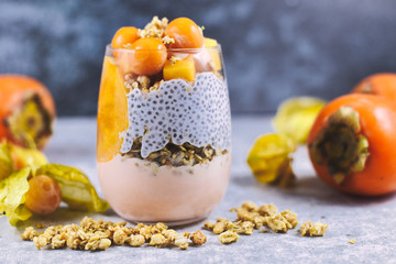 Healthy layered smoothie in glass with chia seeds pudding, mixed with granola and topped with orange persimmon and physalis fruits 