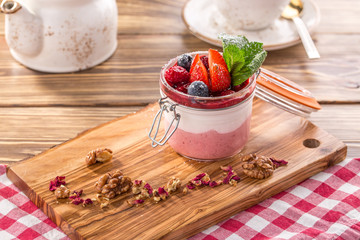 Layered dessert with strawberry and cream cheese panna cotta in glass jar on wooden table