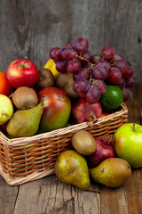 Fruit basket with different fruits. Vitamin set of a healthy diet. Fruit isolated on a gray background. Large set of fruits on a wooden kitchen table. Bananas, apples, pears, pomegranate, tangerine.