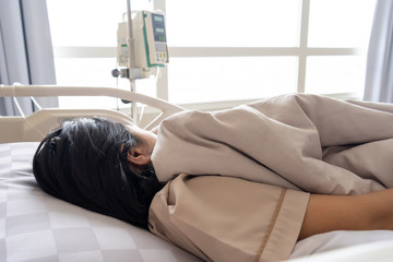 Young woman patient lying on bed while closing her eyes in hospital feeling sad and depressed worried. Disease feeling sick in health care and clinical attention concept.