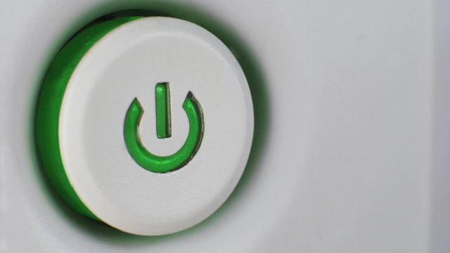 Macro, finger presses the power button on computer equipment to start. Electricity consumption. Man turns on the device with green, blue, red light.