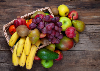 Fruit basket with different fruits. Vitamin set of a healthy diet. Fruit isolated on a gray background. Large set of fruits on a wooden kitchen table. Bananas, apples, pears, pomegranate, tangerine.