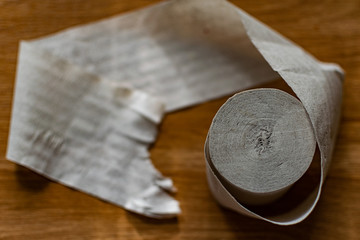 A roll of clean, plain toilet paper, cheap quality, dirty color, lies on a brown wooden table,...