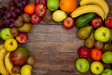 Fruit background with place for text. Different fruits assorted on a wooden table. Vitamin food. Apples, pears, bananas, oranges, kiwi, mango, avocado. A set of healthy food. Frame of fruits. 