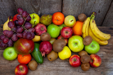 Fruit basket with different fruits. Vitamin set of a healthy diet. Fruit isolated on a gray background. Large set of fruits on a wooden kitchen table. Bananas, apples, pears, pomegranate, tangerine.