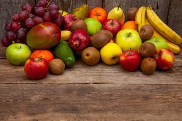 Naklejka na ściany i meble Fruit basket with different fruits. Vitamin set of a healthy diet. Fruit isolated on a gray background. Large set of fruits on a wooden kitchen table. Bananas, apples, pears, pomegranate, tangerine.