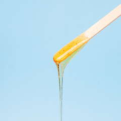 liquid yellow wax or sugar paste for depilation drains from the stick on blue background. The...