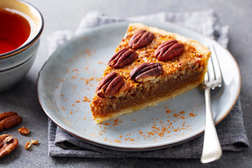 Pecan pie slice on a plate with cup of tea. Grey background. Close up.