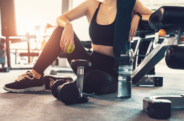 Fototapeta na wymiar Woman exercise workout in gym fitness break and relax. Hands holding apple fruit after training sport with dumbbell and water bottle beside her.