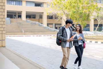 high school students hold book and laptop talking and laughing in a hallway between classes