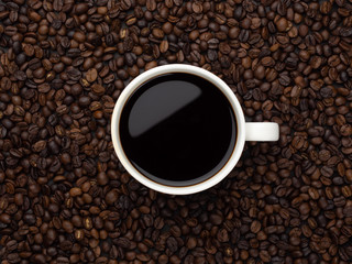 Close-up and top view of hot black coffee in white coffee cup on roasted coffee beans background with area for copy space