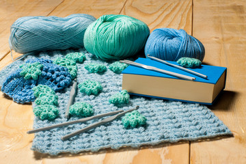 Knitting accessories. On rustic wooden background three balls of yarn and plastic grey hooks, associated blue-green napkin with decor in form of flowers. Concept of hand knitting and crafts