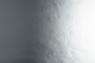 Silver background of real silver paper, illuminated by a soft light from the right, slightly creased.