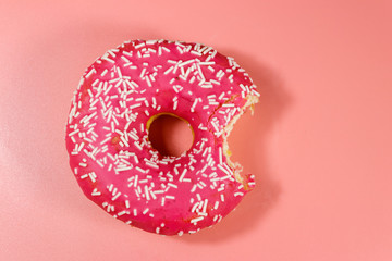 Bitten tasty pink donut on pink background. Top view