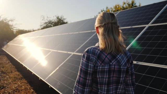 Rear view of woman walks along the solar panels of a small home solar power plant