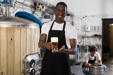 Fototapeta na wymiar African american man brewer in apron standing with glass of beer