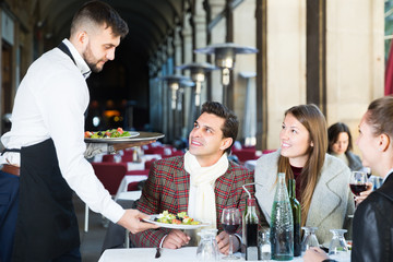 Smiling waiter serving guests at terrace restaurant