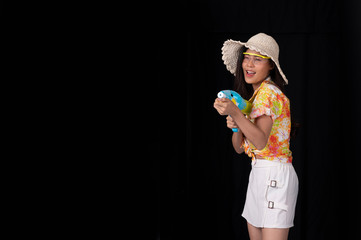 Portrait cheerful young asian woman with red glasses holding plastic water gun on balck background. Songkarn festival, Thailand. Thai New Year's Day. Isolated black  background.