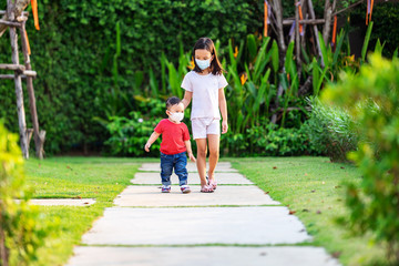 Fototapeta na wymiar Sister and brother together walking at the park walking with wearing a dust mask protect for PM2.5 and as protection new virus COVID-19.
