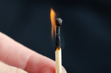 Burning match in hand against a black background. Close-up shot