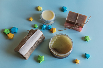 Spa cosmetics, flower soap, handmade sugar scrub with coconut oil in a glass jar, washcloth, face cream and nail file for grinding the skin of the feet on a blue background