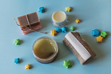 Spa cosmetics, flower soap, handmade sugar scrub with coconut oil in a glass jar, washcloth, face cream and nail file for grinding the skin of the feet on a blue background