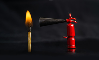 Tiny fire extinguisher close to a burning match against a lit black background, macro shot