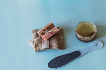 Spa cosmetics, flower soap, handmade sugar scrub with coconut oil in a glass jar, washcloth and file for grinding the skin of the feet on a blue background
