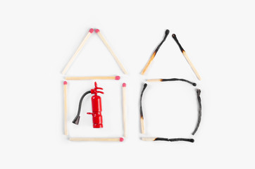 Two houses made of burnt and unburned matches with a miniature fire extinguisher inside the undemaged one. Fire insurance idea