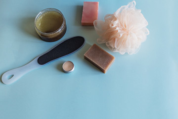 Spa cosmetics, flower soap, handmade sugar scrub with coconut oil in a glass jar, washcloth, face cream and nail file for grinding the skin of the feet on a blue background