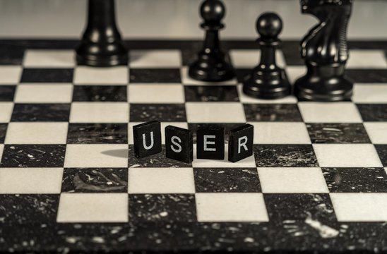 The concept of User represented by black and white letter tiles on a marble chessboard with chess pieces