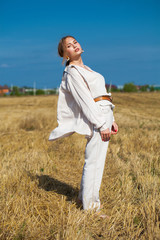 Young woman in a beige suit posing on a background of haystacks in a cut field.