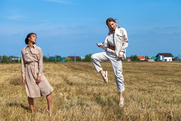 Two girls in a beige suit posing on a background of wheat in a cut field