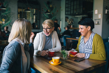 mid aged woman friends talking and drinking coffee in cafe