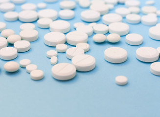 Heap of white pills, tablets, capsules on blue background. Drug prescription for treatment medication health care concept wth copy space.