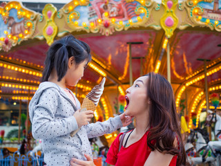 happy asia mother and daughter have fun in amusement carnival park with farris wheel and carousel background