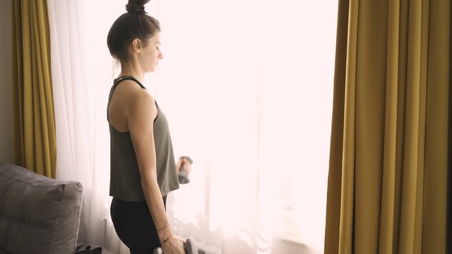 Slim beautiful girl lifting dumbels at home. Lifting weights 