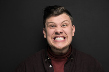 Portrait of young grimacing man isolated on gray background