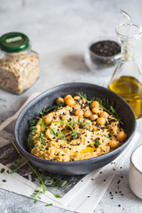 Chickpeas hummus in the black bowl decorated with sesame seeds and chickpeas greens. Vegan recipes, plant-based dishes. Green living concept. Organic food. Vegetarian