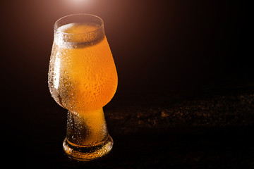 Beer. Cold Craft light Beer in a glass with water drops on the wooden table over the black background.