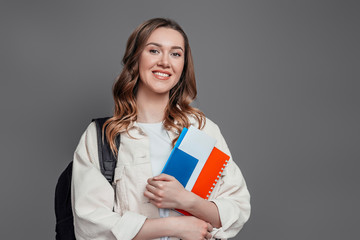 Happy girl student holding backpack, book, notebook, passport isolated on a dark grey background,...
