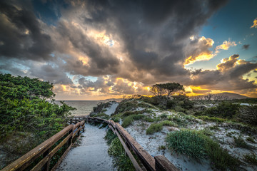Dark clouds over a wooden boardwalk in Maria Pia beach at sunset