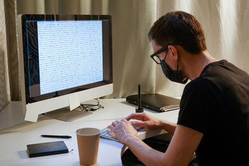 Fototapeta na wymiar Hacker in glasses and a mask in front of the monitor. A young man writes a program code.
