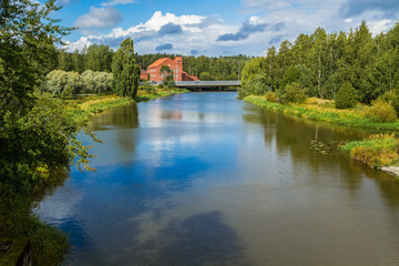 Naklejka na ściany i meble The landscape of the Vantaa river in Vakhakaupunki. Lonely brick house in the distance. Sky reflection in the water.