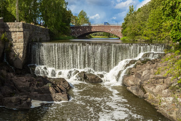 Obraz premium The picturesque view of Vanhakaupunki, the oldest part of Helsinki. The brick bridge over the Vantaa river, artifical waterfall of the hydroelectric power station