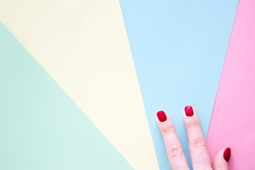 Fingers of woman with red manicure on color paper background