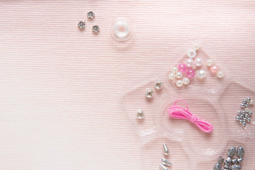 background of pink fabric with accessories for weaving with beads with a container for beads