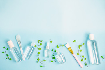Green cosmetics. Organic cosmetics frame background. Cosmetic transparent bottles with liquid, cosmetic brush, plant twigs with green leaves on a blue background. Top view, copy space, flat lay
